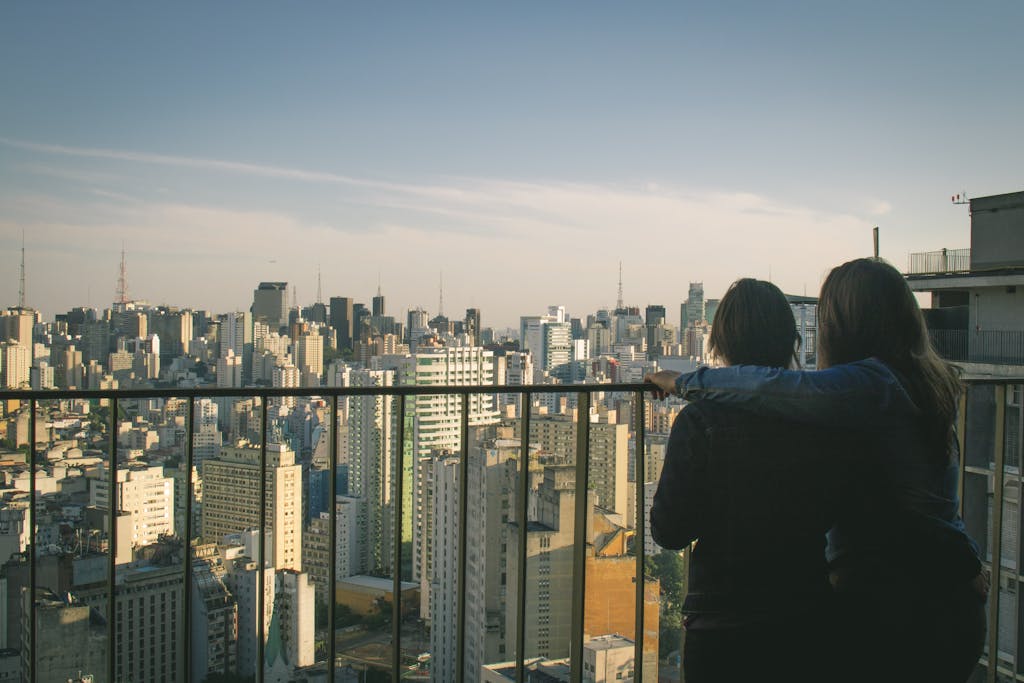 A couple embraces while viewing a vibrant cityscape from a rooftop.