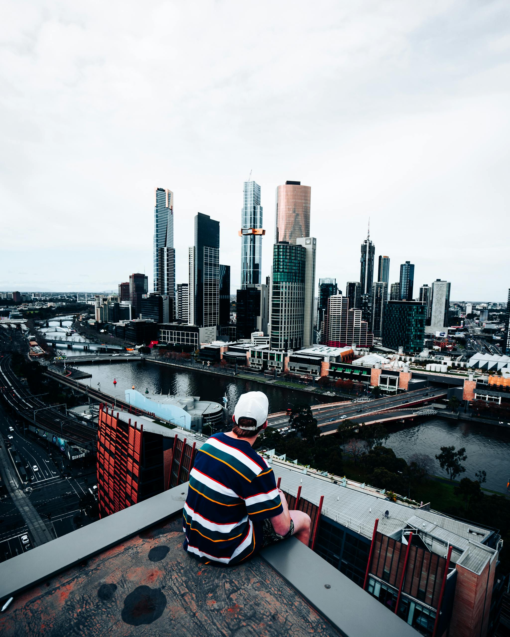 A man on a rooftop enjoys a scenic view of Melbourne's cityscape with skyscrapers and the Yarra River.