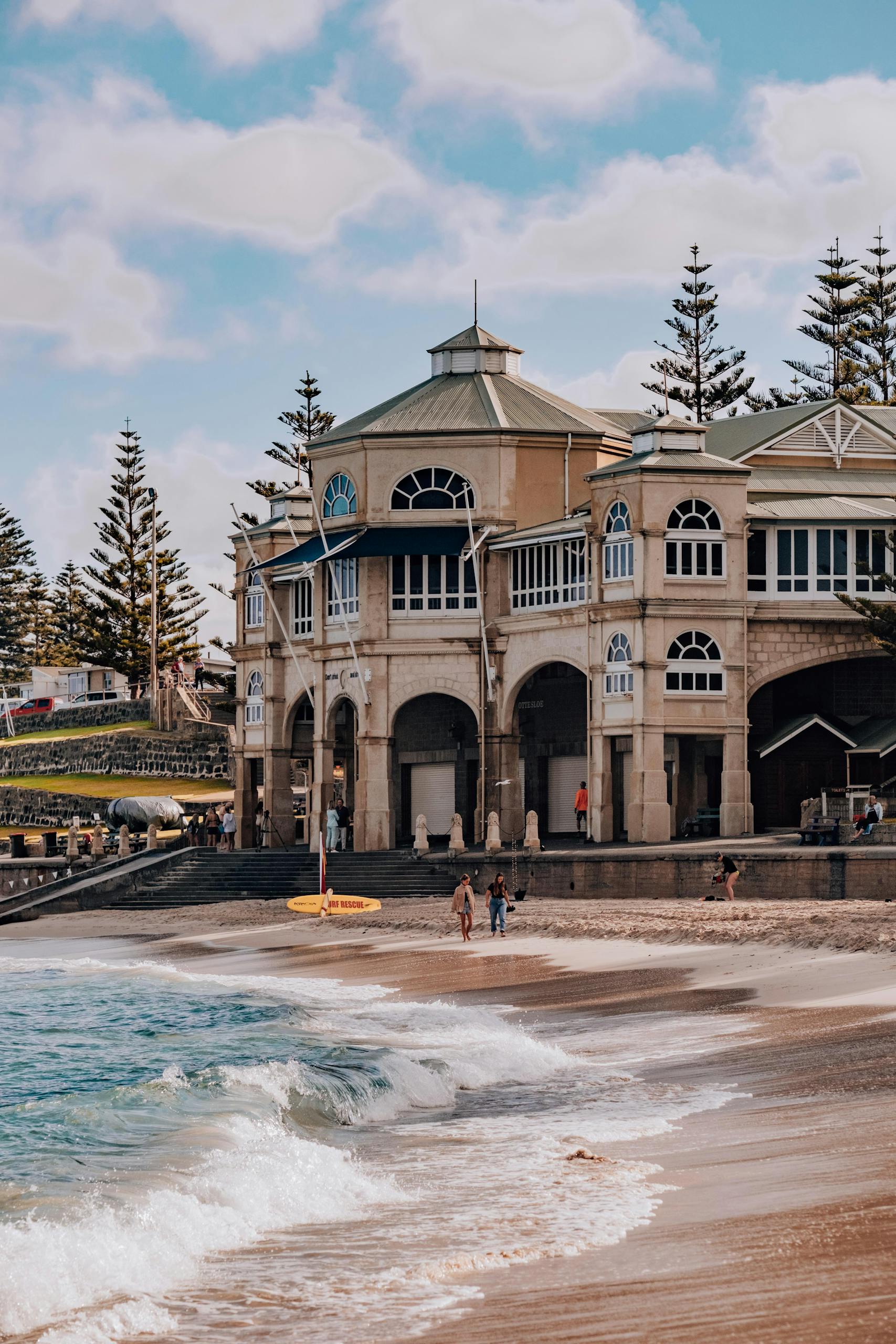 Beachfront view of historic building at Cottesloe Beach, WA. Waves washing ashore under blue sky.