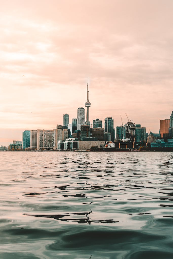 Captivating view of Toronto skyline with CN Tower reflecting on Lake Ontario at sunset.