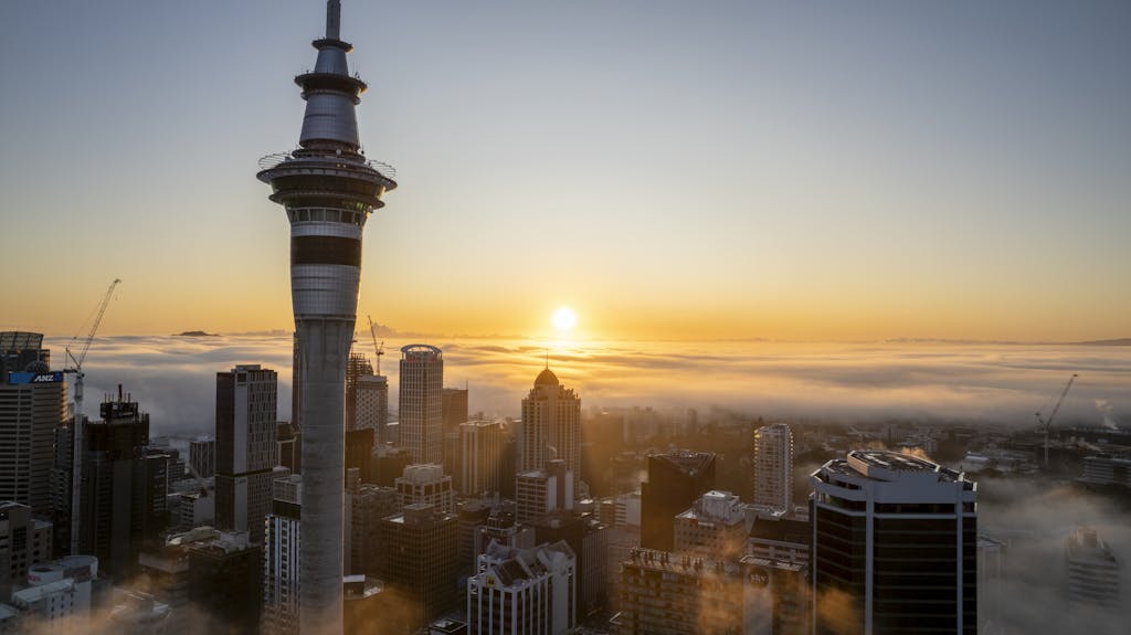 Stunning aerial view of Auckland cityscape at sunrise, featuring iconic Sky Tower enveloped in morning fog.